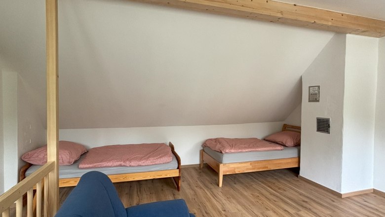 Single beds in open hallway@Ferienhaus Hofer, © Wiener Alpen Two single beds with pink bed linen in a room with wooden floor and blue couch.