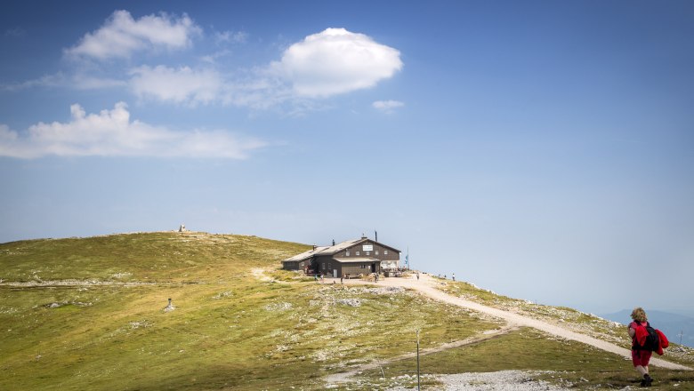 Viewpoint Fischerhütte Schneeberg, © Wiener Alpen, Foto: Franz Zwickl A mountain hut on a hill with a blue sky and clouds in the background.