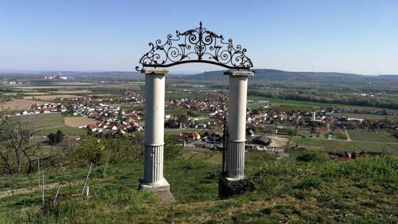 Heinz Conrad Gate, © Roman Zöchlinger Two columns with an ornate arch on a hill overlooking a village and fields in the background.
