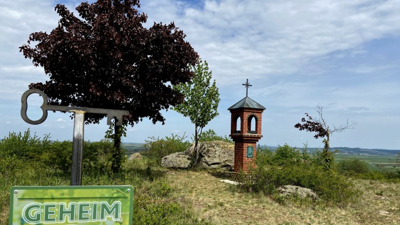 Lord's seat Etzmannsdorf, © Weinstraße Weinviertel A sign with the inscription 'Geheim Tipp' in front of a small brick tower with a cross on a hill.