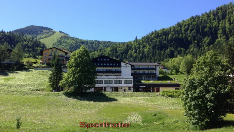 Sporthotel am Ötscher, © zVg A sports hotel in a green mountain landscape with a blue sky.