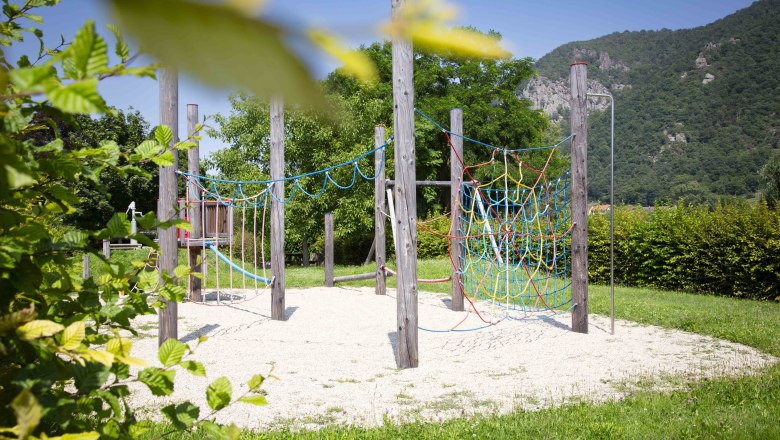 Adventure playground in Joching, © Donau NÖ Tourismus_Barbara Elser An adventure playground with climbing frames and nets in a green setting with mountains in the background.