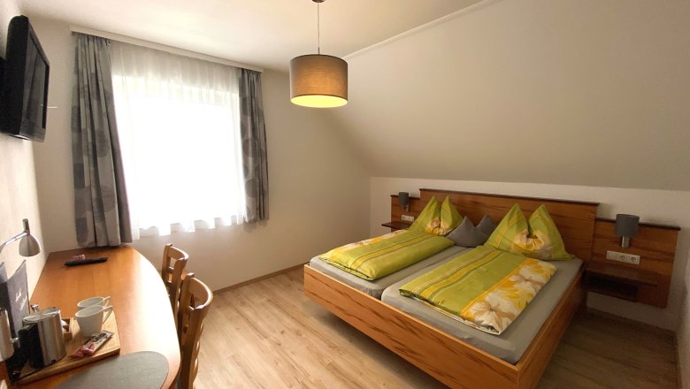 Double room, © Trachsler A cozy double room with a double bed, desk, chairs and a TV on the wall.