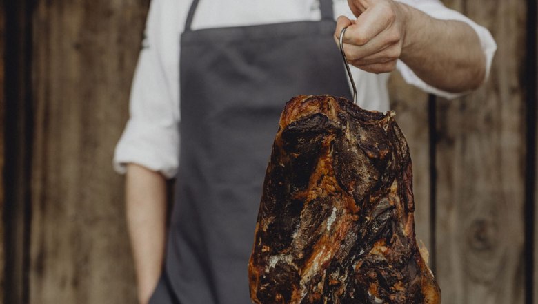 Home-smoked Emmerberger smoked ham, © Niederösterreich Werbung/Sophie Menegaldo Person holding smoked ham on a hook.