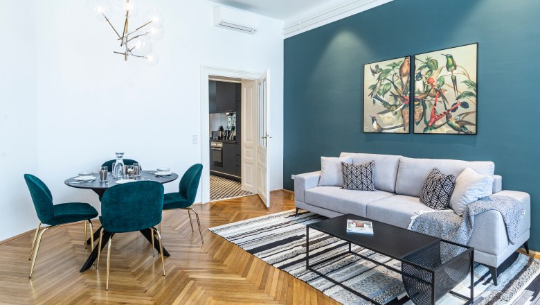 Apartment, © Astrid Bartl Modern living room with gray sofa, dining table and art on the wall.