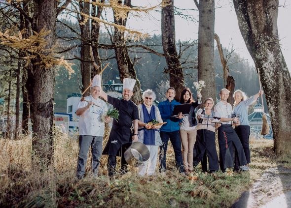 Berghof team, © Gasthof Berghof A group of people in cooking clothes stand happily in a forest.