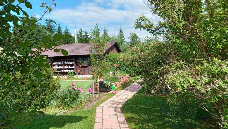 Visual axis in the garden, © Natur im Garten Garden with path, flowers and wooden hut in the background.