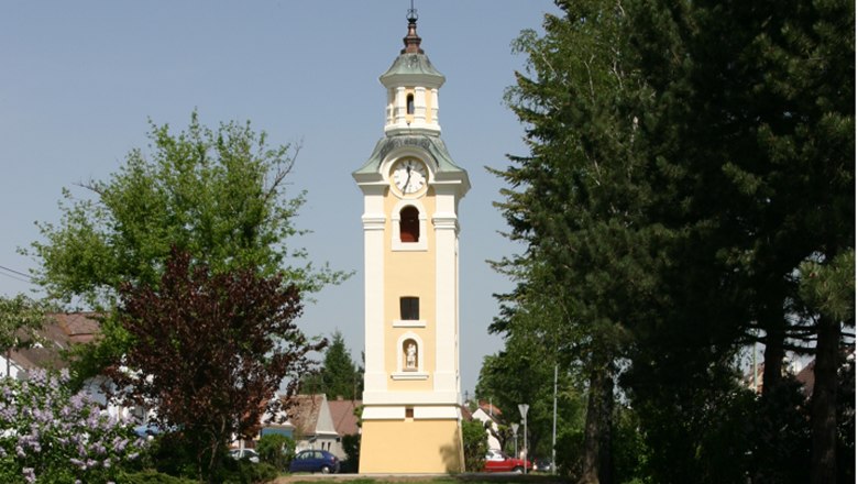 Hohenau, © Gemeinde Hohenau/ March Yellow church tower with clock in Hohenau, surrounded by trees.