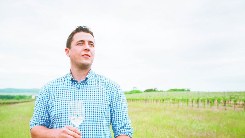 Winemaker Lukas Frotzler, © Weingut Frotzler Man in plaid shirt holding wine glass in vineyard.