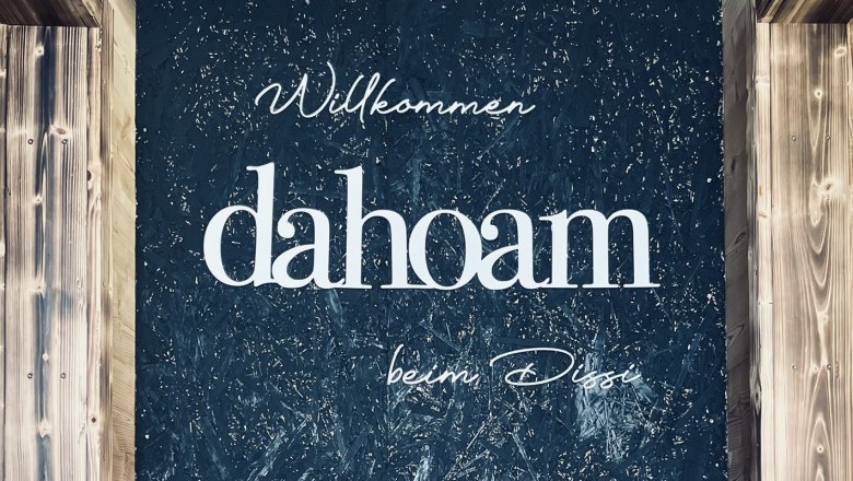 Welcome to "dahoam", © Anita Gradwohl, dahoam Wall with lettering 'Willkommen dahoam beim Dissi' and decoration.