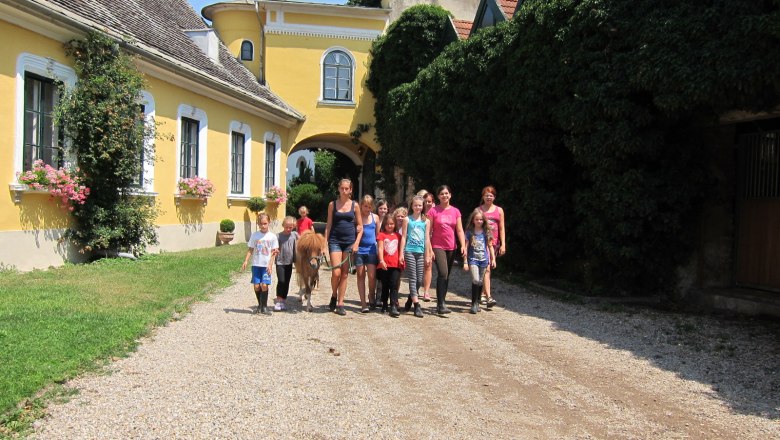 Paradise for children, teenagers and adults, © rgf Group of children and adults with pony in front of yellow building.