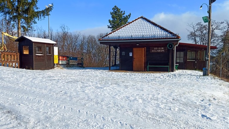 In between a little refreshment in the cozy ski hut, © Fritz Weiss Snow-covered ski club hut with wooden huts and trees in the background.