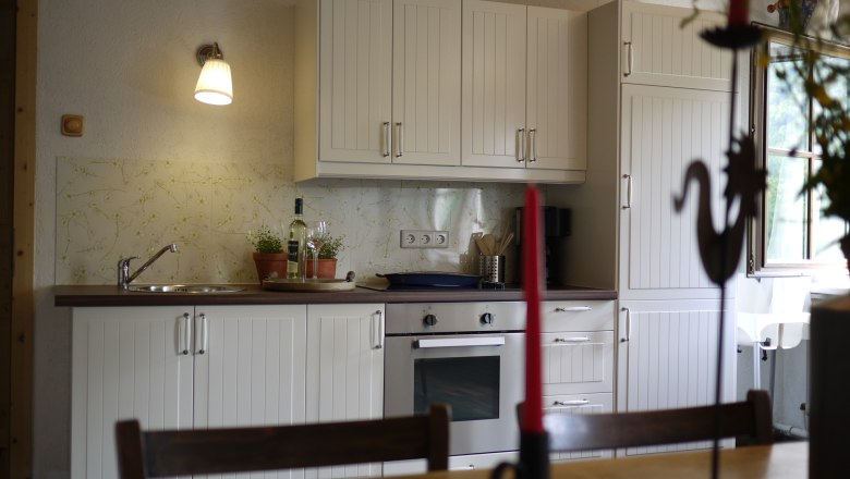 Rinntaverne, © Rinntaverne Kitchen with white cupboards, stove and sink, decorated with plants and a bottle of wine.