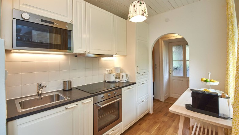 Top 5 - Kitchen, © VP FeWo OG Modern kitchen with white cupboards, wooden floor and appliances such as oven and microwave.