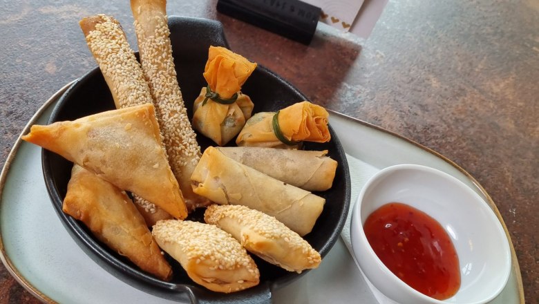 Cafe Herzstück, © Cafe Herzstück_Stephanie Kirschner Various fried snacks on a plate with dip and café centerpiece menu in the background.
