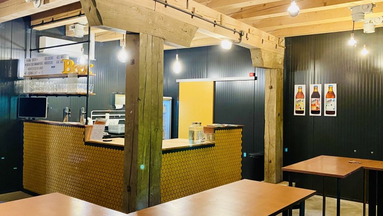 Store, © Hopfenspinnerei Interior view of a modern café with wooden beams, bar counter and high tables.