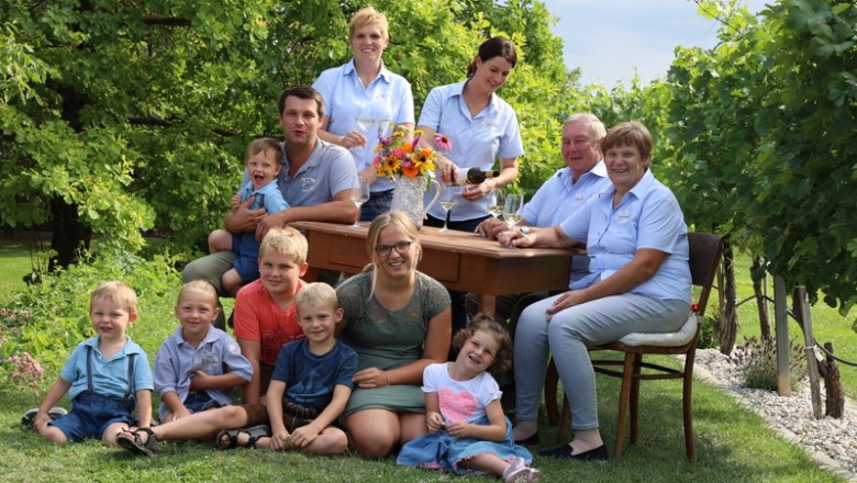 Dunkl family, © Manuela Winkler A family sits and stands around an outdoor table, surrounded by trees and grass.