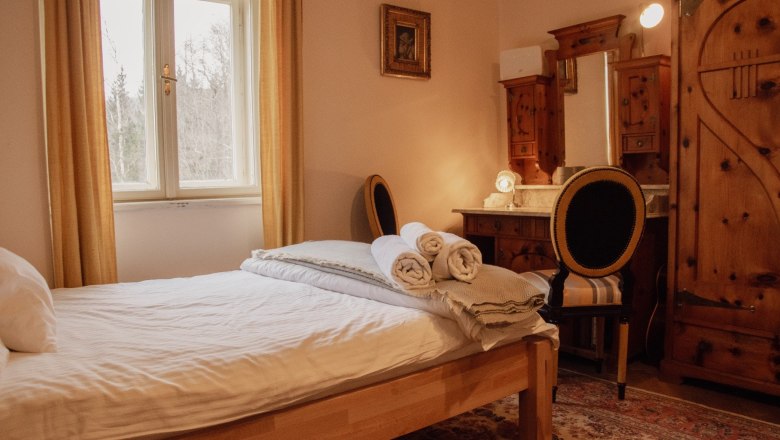 Orlet on the Rax, © Sofia Orlet Cozy bedroom with wooden furniture and a window with curtains.