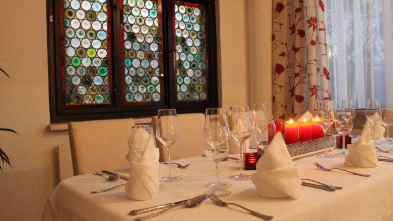 Hotel Stadt Melk - Verandatisch, © © Hotel Stadt Melk Elegant table with white tablecloths, wine glasses and red candles in front of a colorful window.