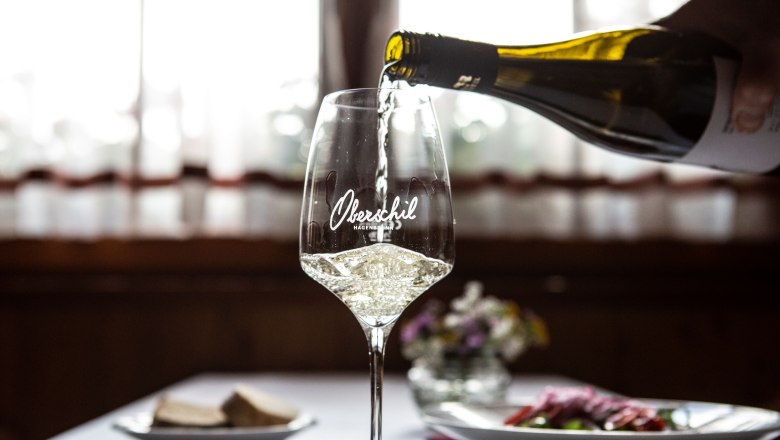 Wine tavern Oberschil, © Astrid Bartl A glass of white wine is poured, a table laid with flowers in the background.