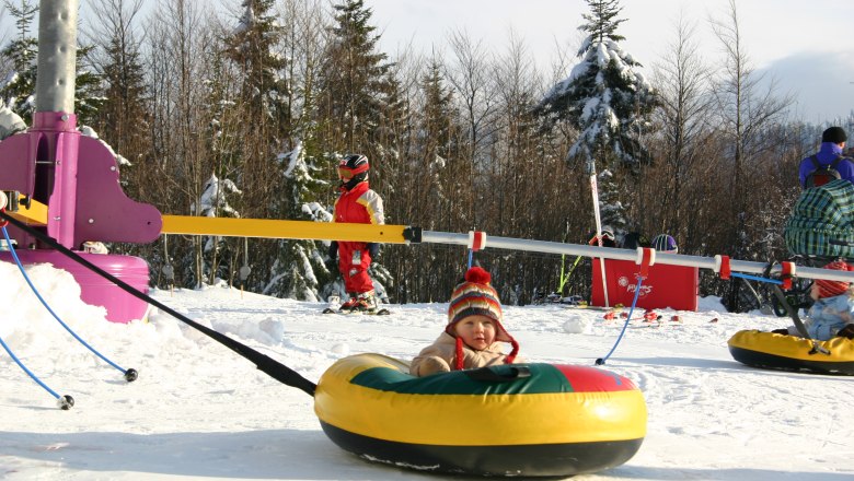Turmkogel, © Gemeinde Puchenstuben Toddler in a colorful snow tire on a snowy hill with other children in the background.