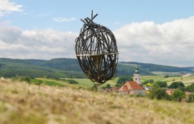 art_in_nature-002125_excerpt__c_nature_in_the_garden_alexander_haiden, © Natur im Garten/Alexander Haiden Metal art installation in a rural landscape with a church in the background.