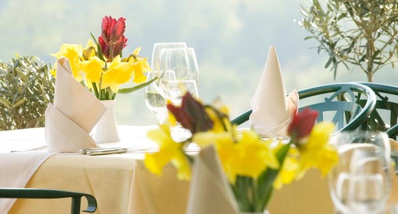 Set table, © F. Bläuel GesmbH An elegantly laid outdoor table with yellow and red flowers, white napkins and wine glasses.