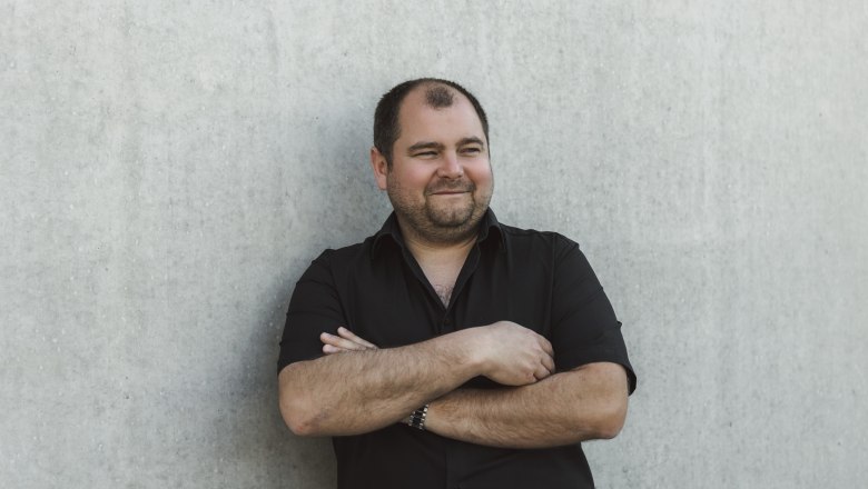 Peter Kerschbaummayr, © Niederösterreich Werbung/David Schreiber Man in a black shirt leaning against a concrete wall.