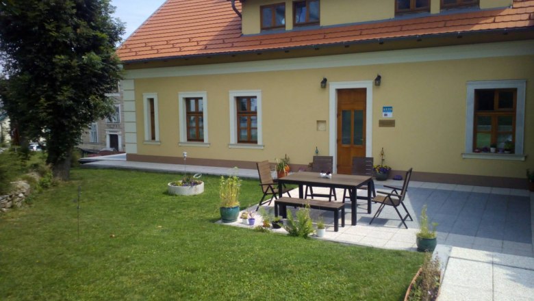 Terrace, © Ildiko Davidne Nagy A yellow house with a red roof and terrace, surrounded by lawns and plants.