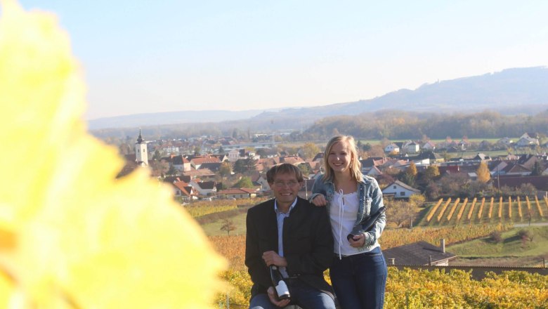 Mittelbach family in the vineyard, © Weingut Mittelbach Two people in a vineyard with a view of a village in the background.