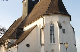 Totzenbach parish church, © Pfarrkirche Totzenbach Totzenbach parish church with clock tower and pointed roof, surrounded by a fence, in daylight.