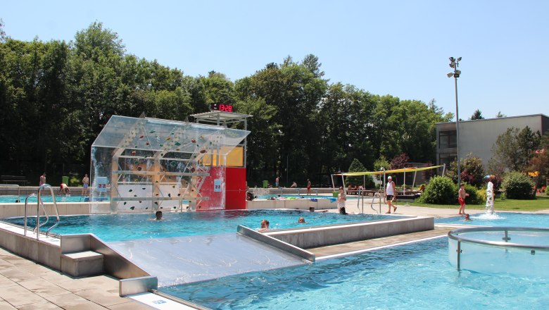 Neunkirchen Recreation Center, © Stadtgemeinde Neunkirchen Outdoor pool with climbing wall, surrounded by trees.