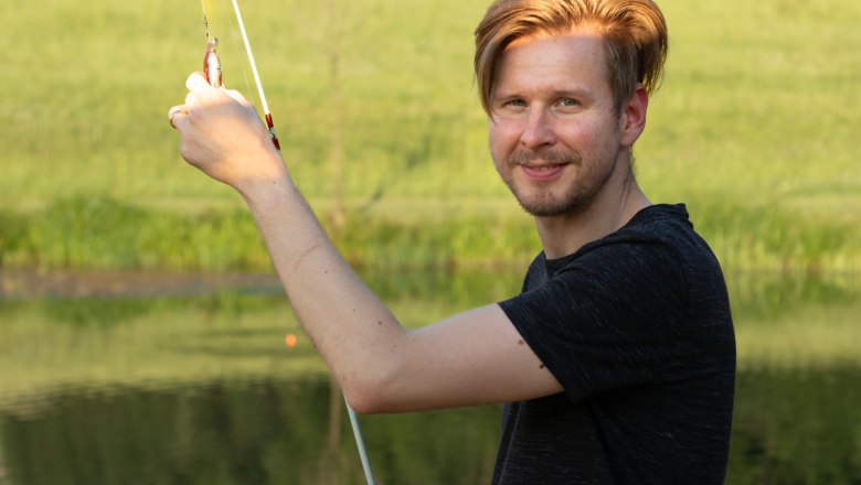 Fishing at the pond, © Familie Moser Man with fishing rod at a pond in front of a green landscape.