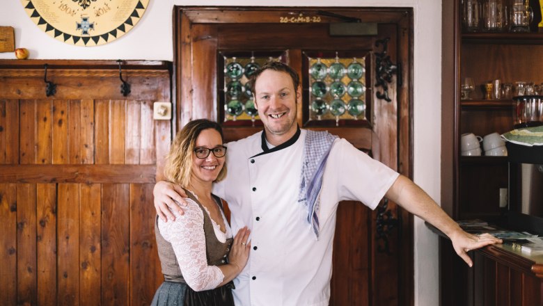 Head chef Christian, landlady Magdalena Donhauser, © Niederösterreich Werbung/ A man in chef's clothes and a woman in traditional dress stand smiling in a rustic room.