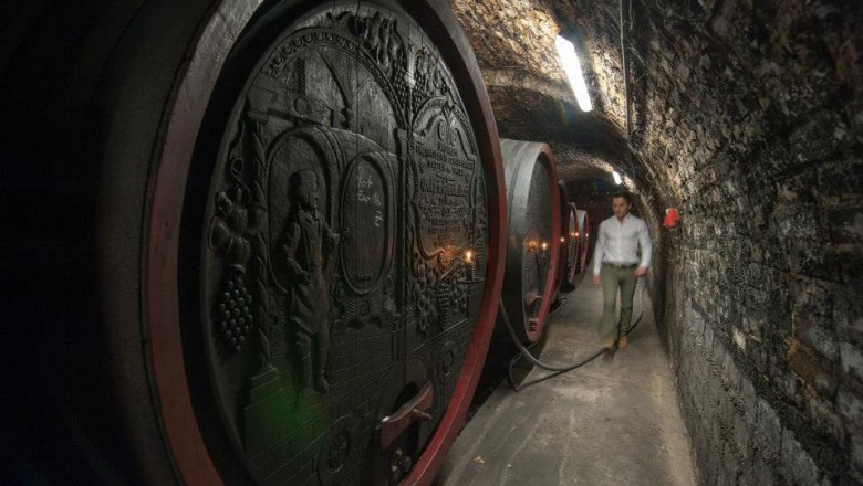 mittelbach-2, © Gottfried Mittelbach A man walks through a wine cellar with large, decorated wooden barrels.
