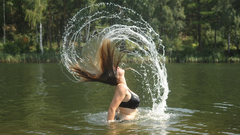Seecamping Langau 3, © Nadine Reinagl Woman throws her hair back in the water, creating a splash of water.