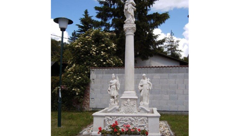 Marian column, © Gemeinde Hauskirchen Marian column with statues and flowers, surrounded by trees and a wall.