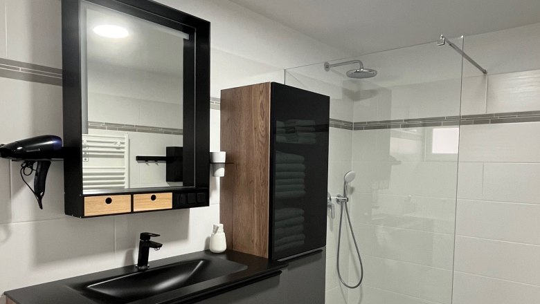 Bathroom, © Jochen Maurer Modern bathroom with black washbasin, mirror, rain shower and gray tiles.