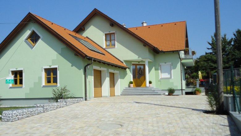 Guest room Rieder, © Fam. Rieder A modern, two-story house with green paint and red roof tiles, surrounded by a paved courtyard.