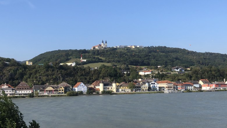 Krummnussbaum landing stage opposite the Maria Taferl basilica, © Donau NÖ Tourismus View of the Maria Taferl basilica on a hill, with houses and a river in the foreground.