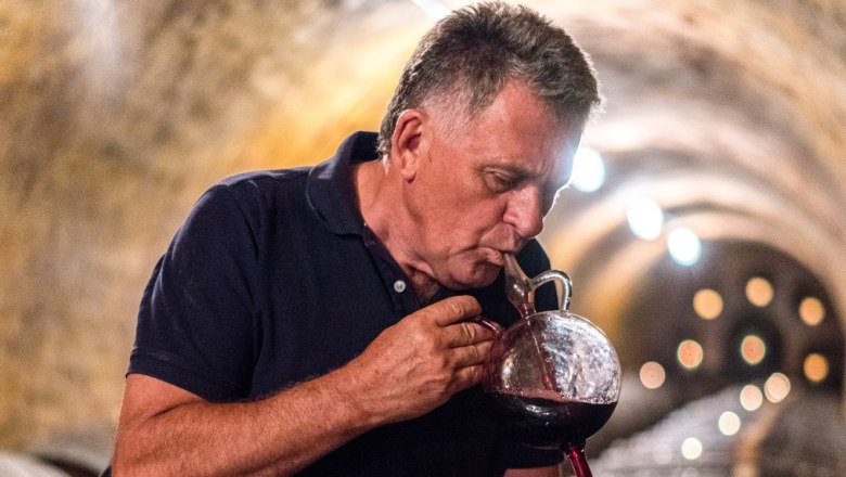 Rudolf Zesch, © Fam. Zesch A man tastes wine from a barrel in a wine cellar.
