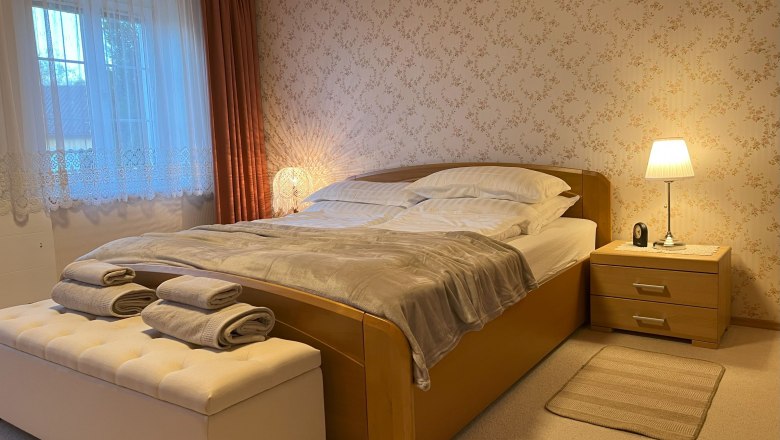 Bedroom, © Waltraud Forstner Cozy bedroom with double bed, bedside lamp and window with curtains.