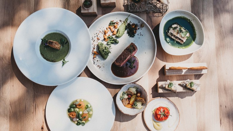Delicacies from the award-winning kitchen, © Molzbachhof Various gourmet dishes on white plates, artfully arranged on a wooden table.