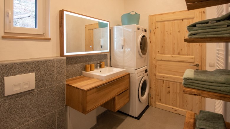 Bathroom, © Silbersberg Cottage Modern bathroom with wooden washbasin, illuminated mirror, washing machine and dryer. Towels on wooden shelves.