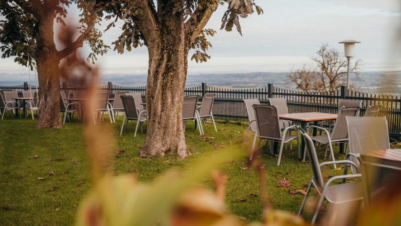 Panoramic view from Linz to Maria Taferl, © Niederösterreich Werbung/Daniela Führer Garden with tables and chairs under trees, overlooking a wide landscape.