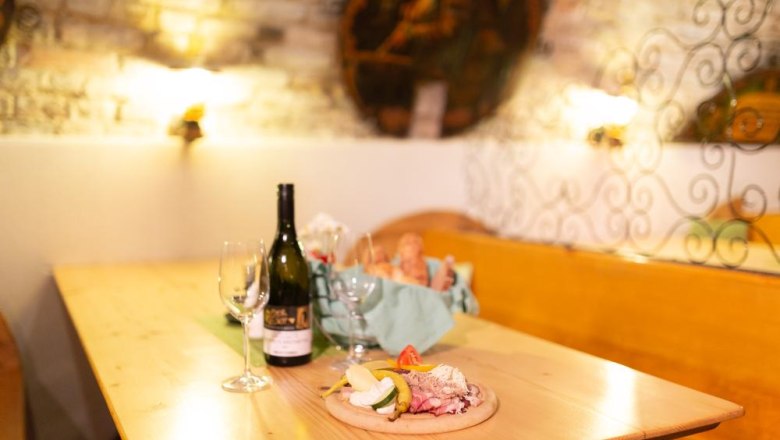 A hearty snack, © Alexander Pfeffel A table in a rustic room with a bottle of wine, glasses and a snack with bread and cold cuts.