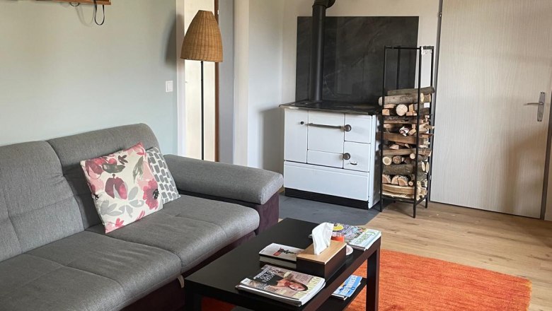 Living room, © Regina Schimmer Cozy living room with grey sofa, coffee table, red carpet and wood-burning stove.