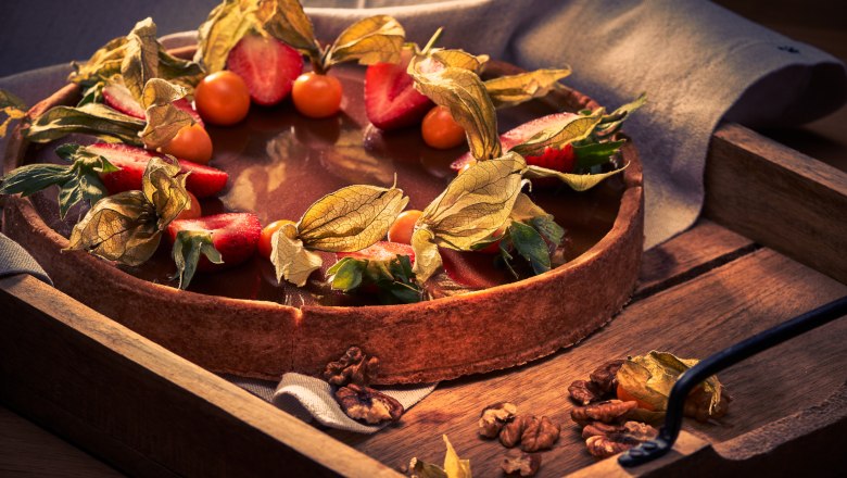 Cake creations, © Niederösterreich Werbung/Andreas Hofer A cake with chocolate icing, decorated with strawberries and physalis, on a wooden tray.