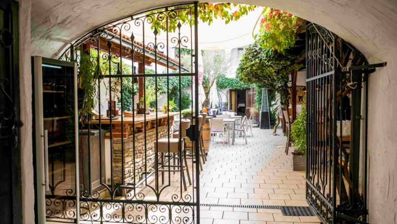 Maximahl arcade courtyard, © Robert Herbst View through a wrought-iron gate into a cozy courtyard with tables and plants.
