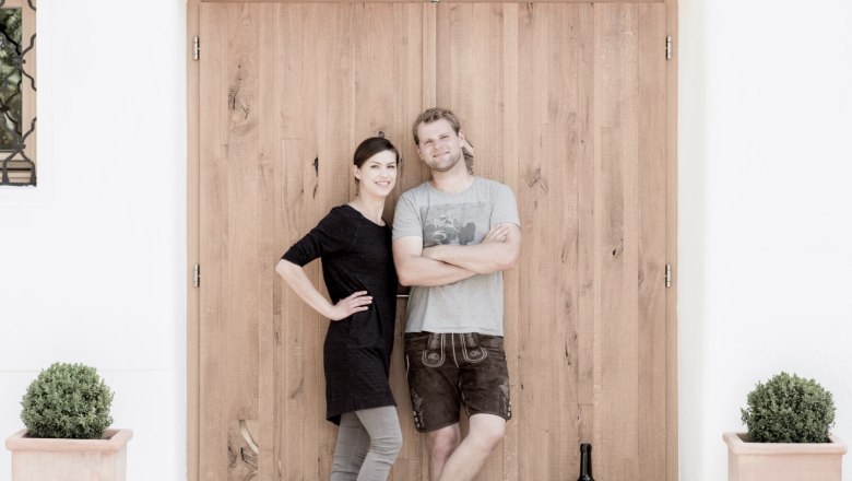 Organic viticulture Weber, © Familie Weber Two people are standing in front of a wooden door, next to a large bottle of wine and plants in pots.